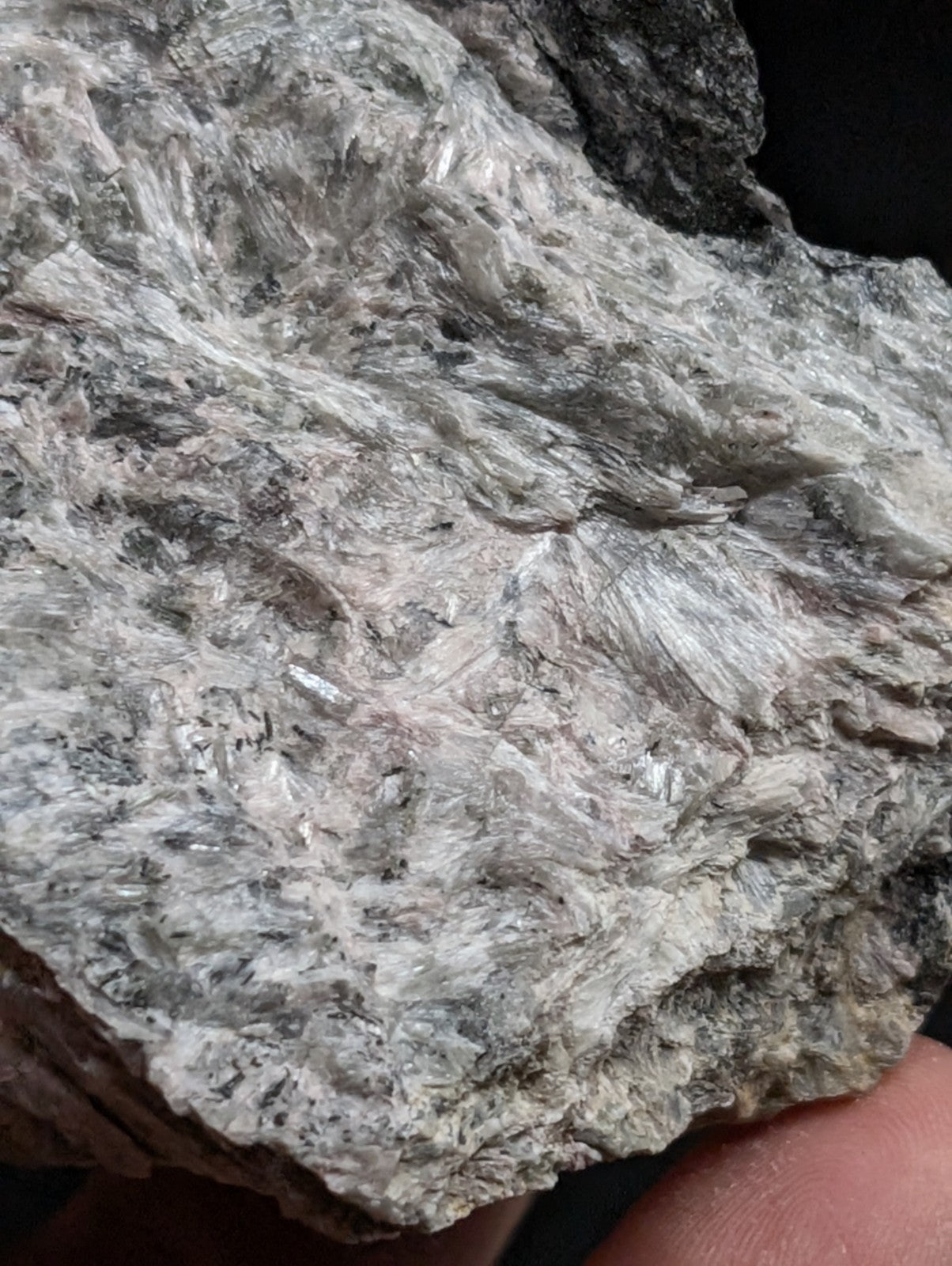 A rough, grayish-white mineral specimen with a crystalline texture and scattered darker inclusions.