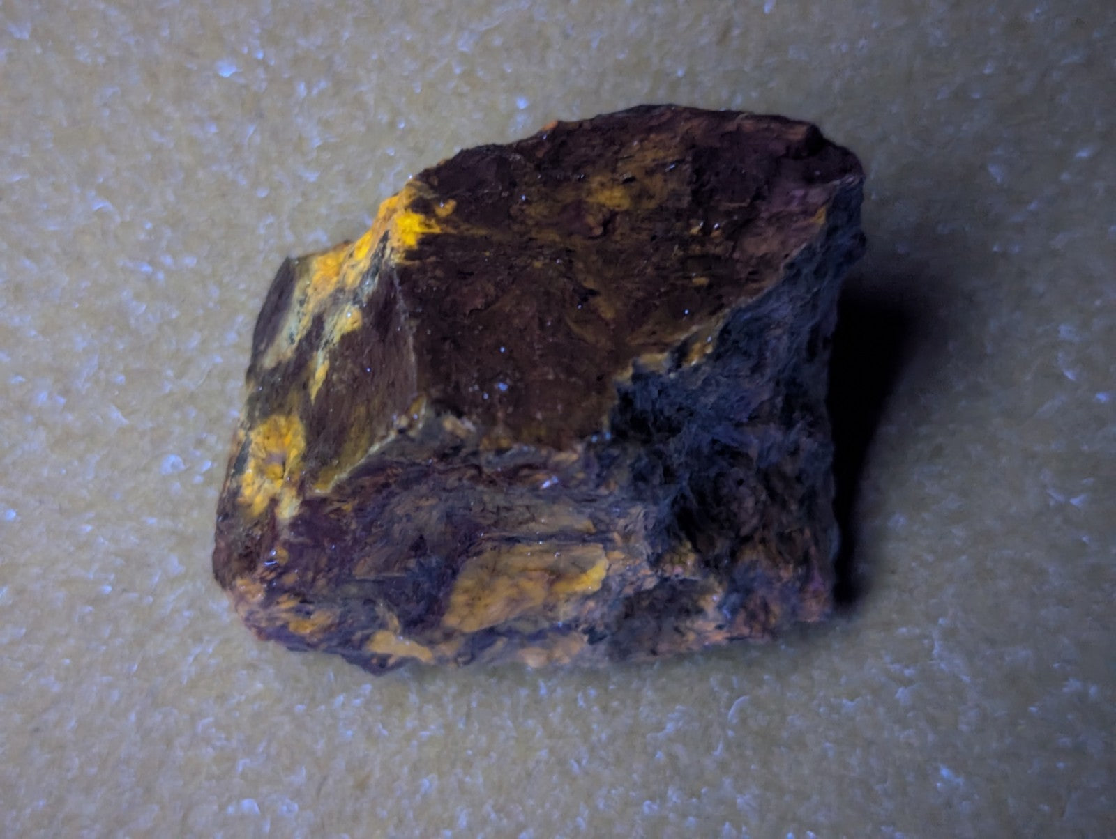 A rugged, irregularly shaped rock with a dark brown base and patches of bright yellow mineral streaks.