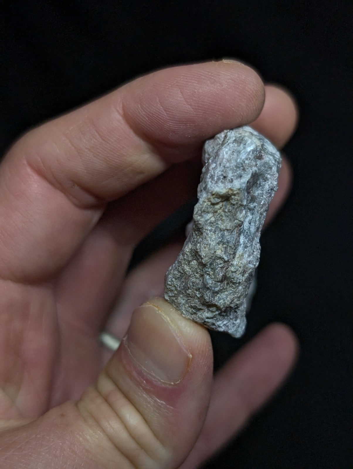 A rough, grayish-white rock with a textured, uneven surface held in someone’s hand.