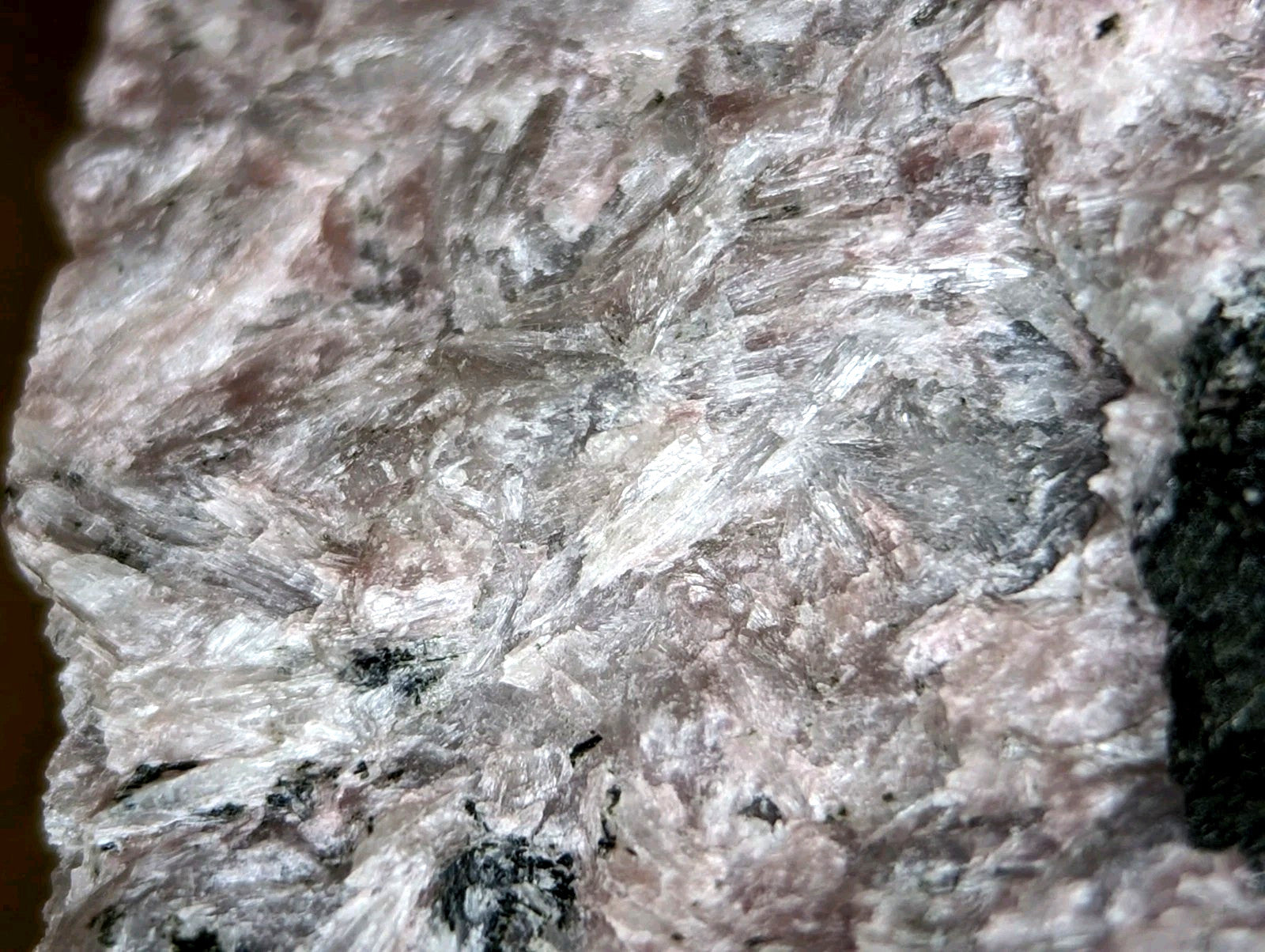 A rough, textured mineral specimen with a mottled pink and gray surface featuring prominent white crystalline streaks.