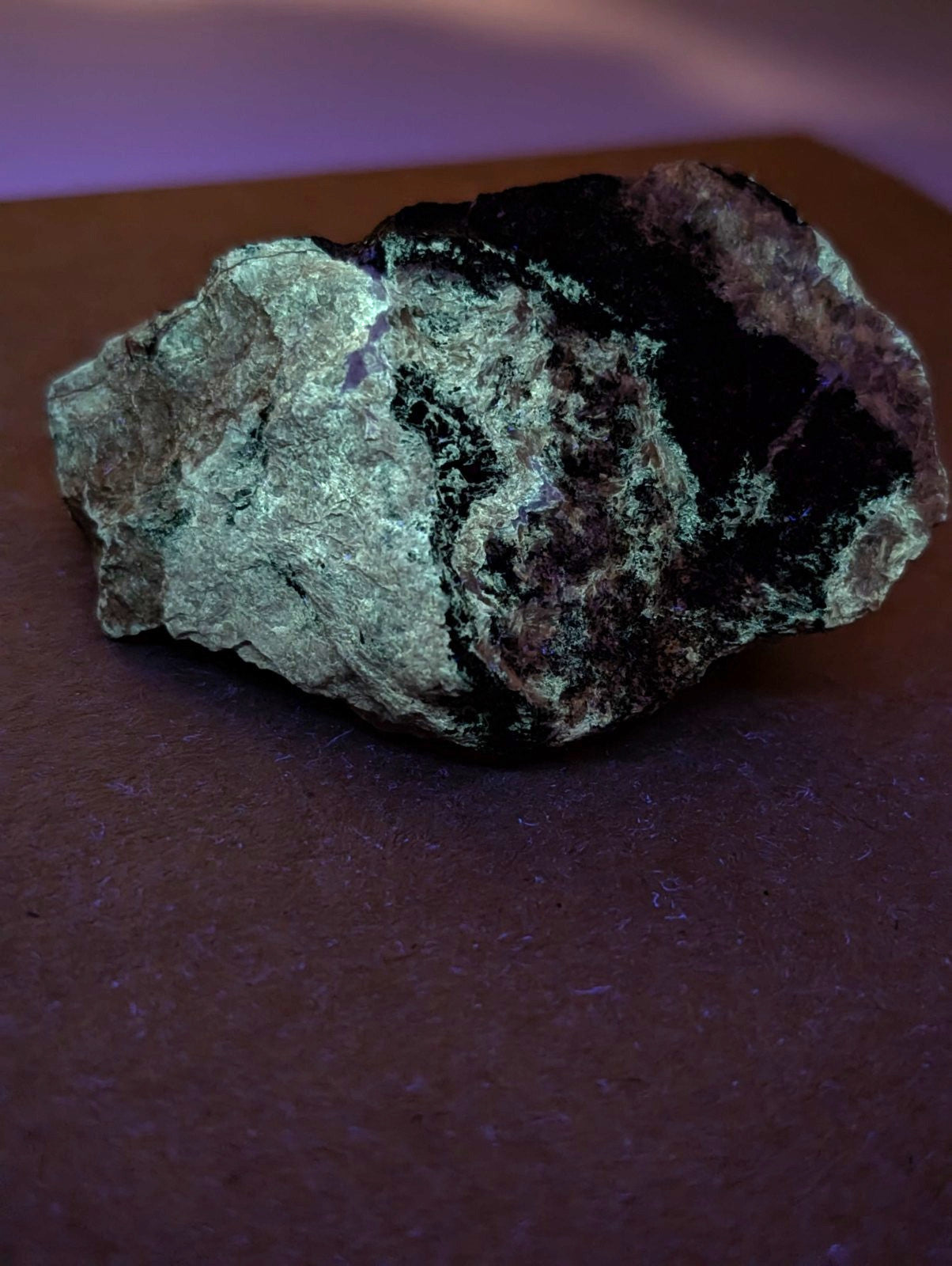 A rugged miserite and wollastonite rock with dark green and black patches under purple lighting from Arkansas usa