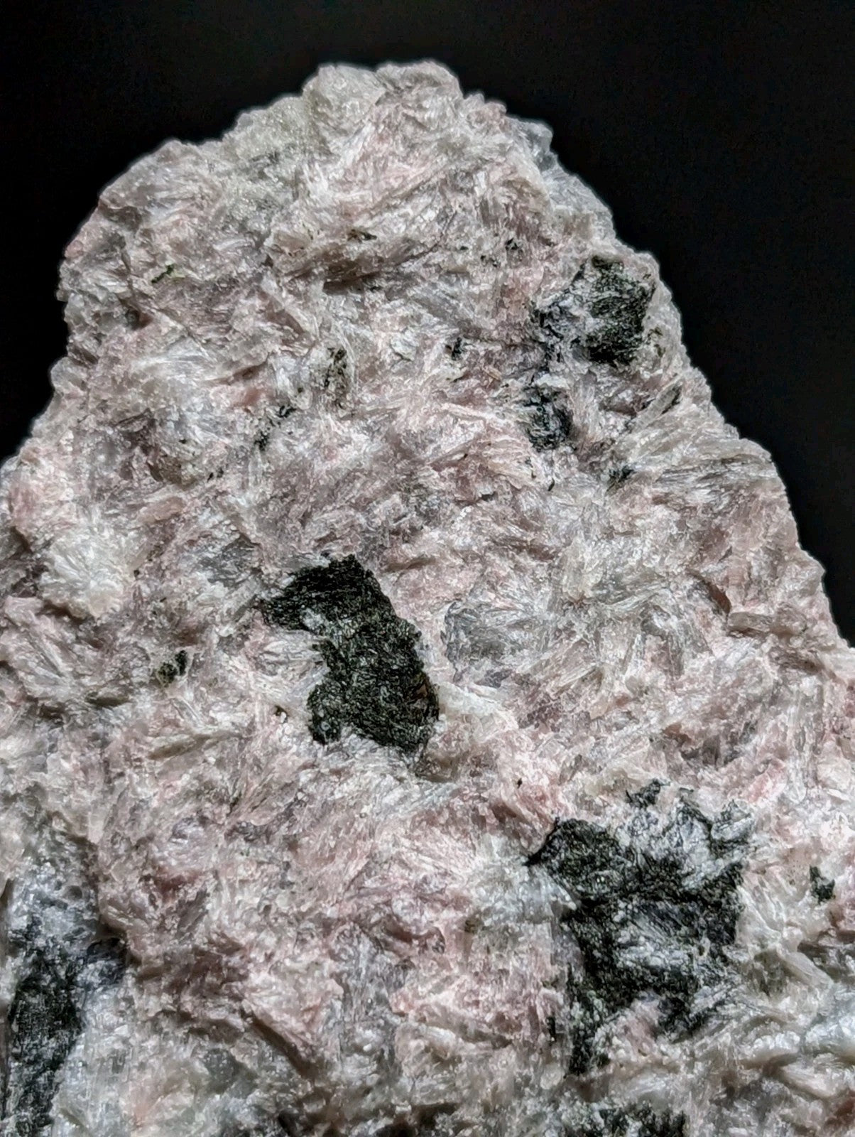 A rough, pinkish-white mineral specimen with embedded dark black inclusions.