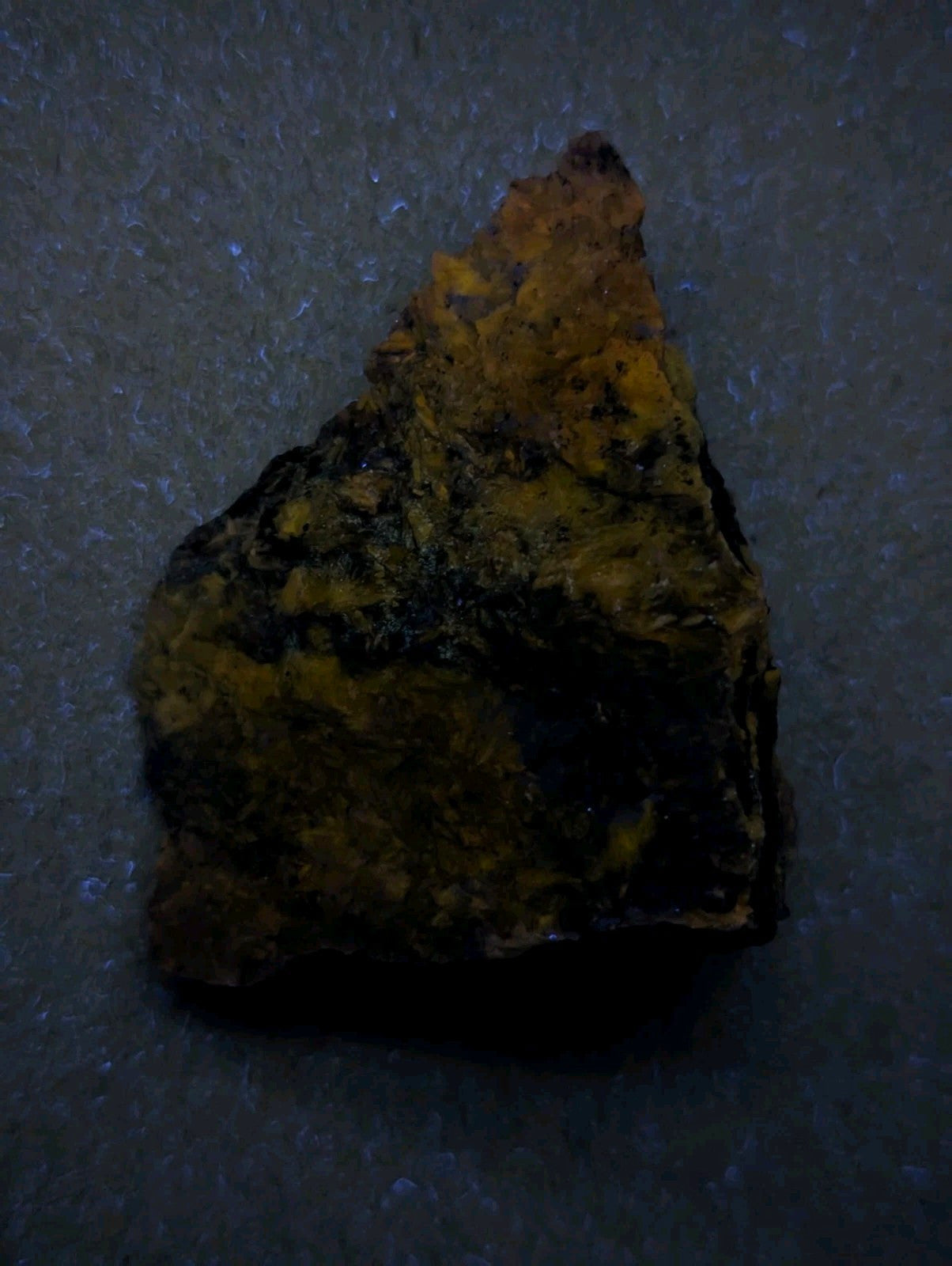 A rough, triangular-shaped mineral specimen with a mottled surface of dark brown and yellowish-orange hues.