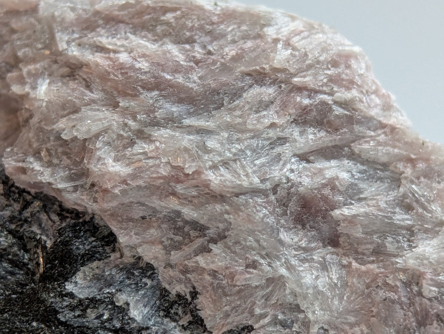 A translucent pinkish-white mineral specimen with a crystalline, fibrous texture and subtle iridescence.