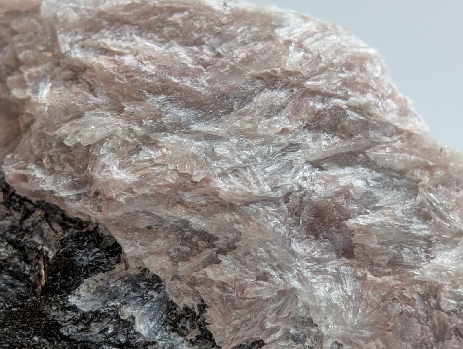 A translucent pinkish-white mineral specimen with a crystalline, fibrous texture and subtle iridescence.