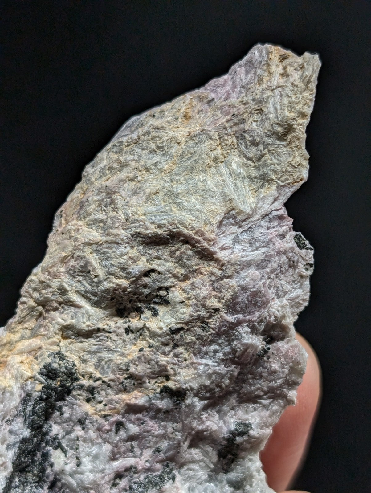 A rough, irregularly shaped rock with a mottled surface of gray, white, and subtle purple hues.