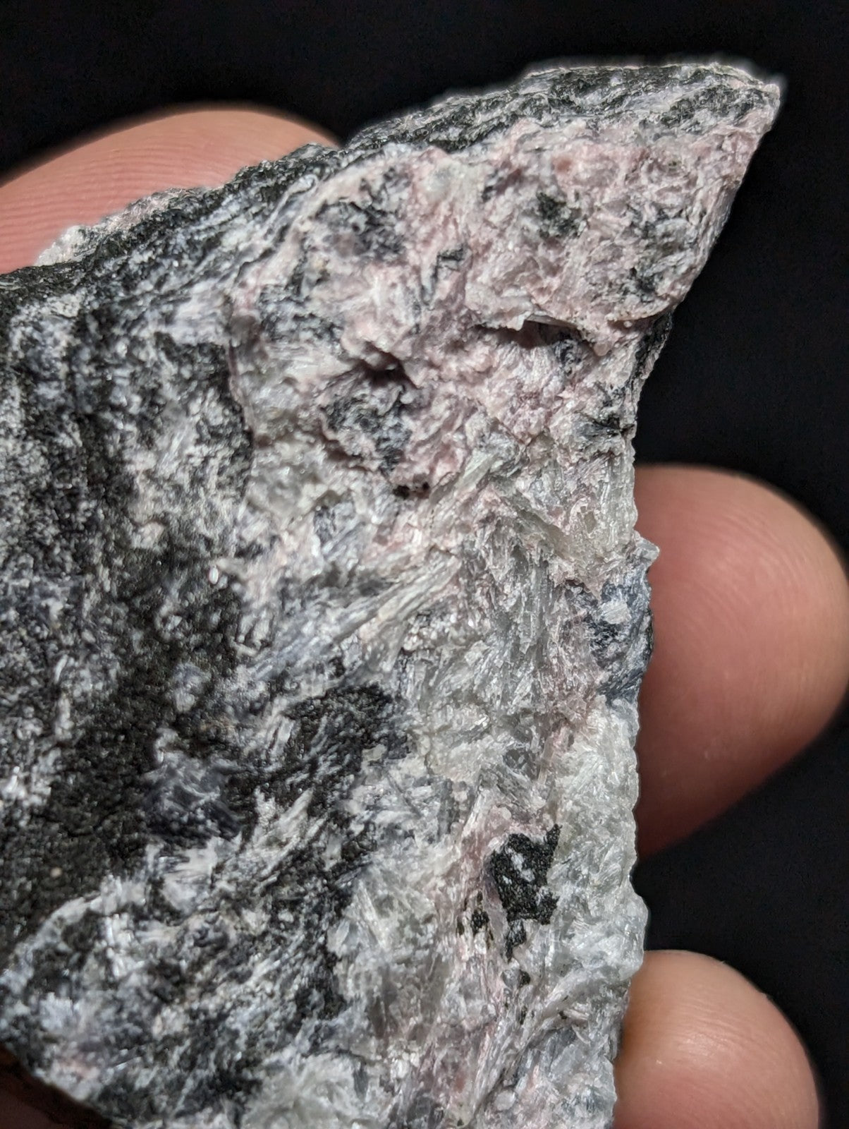 A rough, irregularly shaped mineral specimen with a mottled surface of gray, black, and subtle pinkish hues.