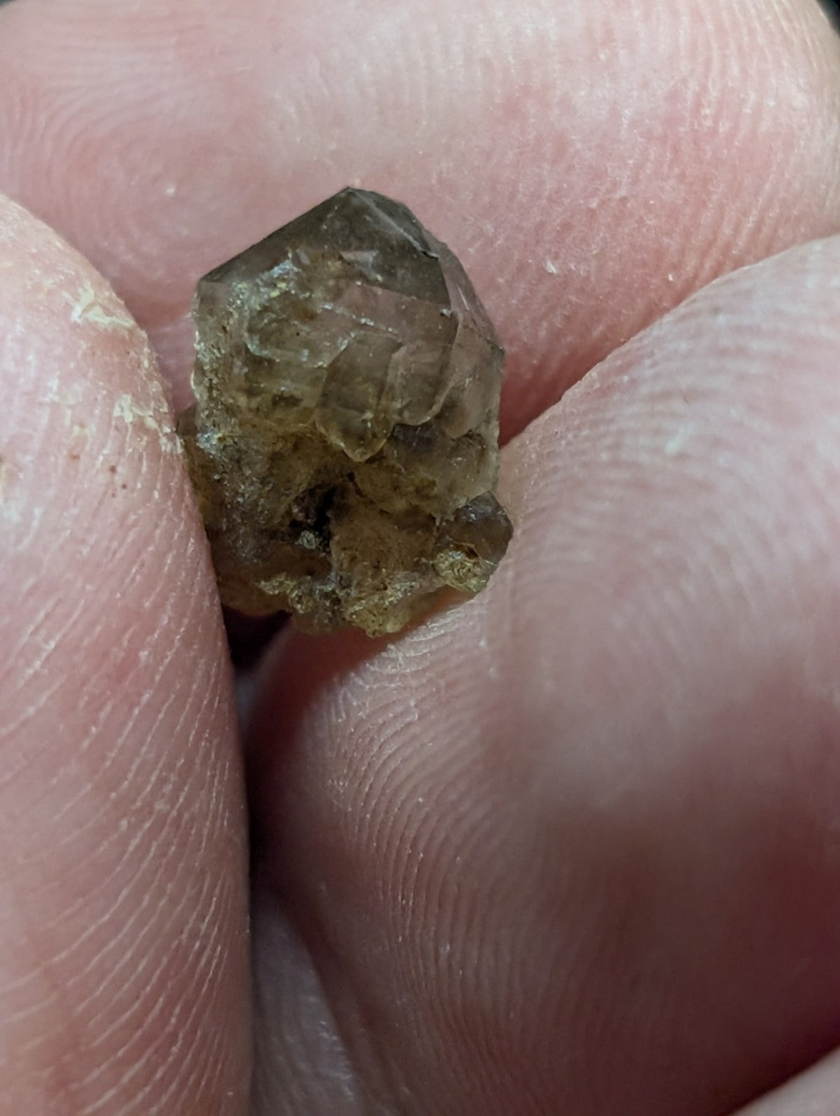 A rough, translucent brownish-green crystal with visible facets and a slightly irregular shape.