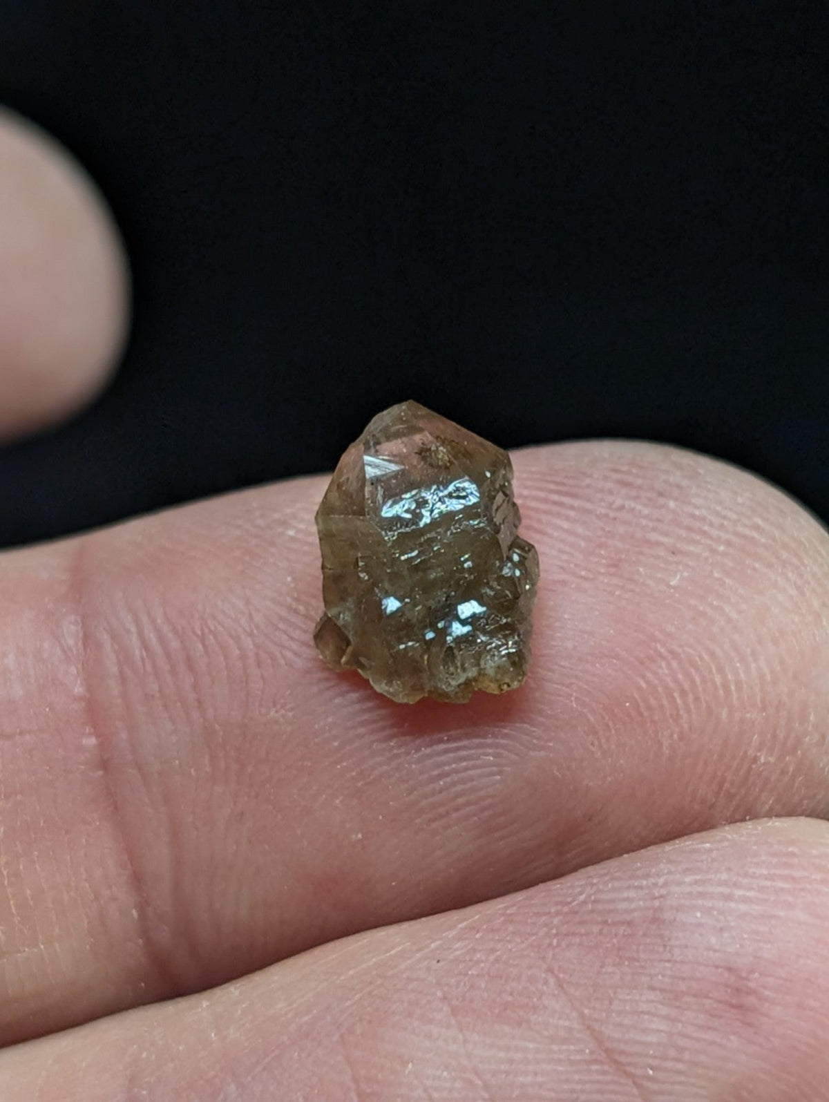 A small, faceted brown crystal with a translucent quality rests delicately on the tip of a finger.