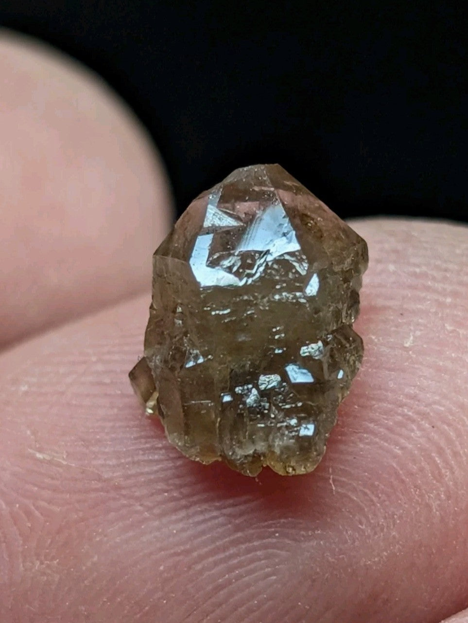 A faceted, translucent brown crystal with a rough, natural texture rests delicately on fingertips.