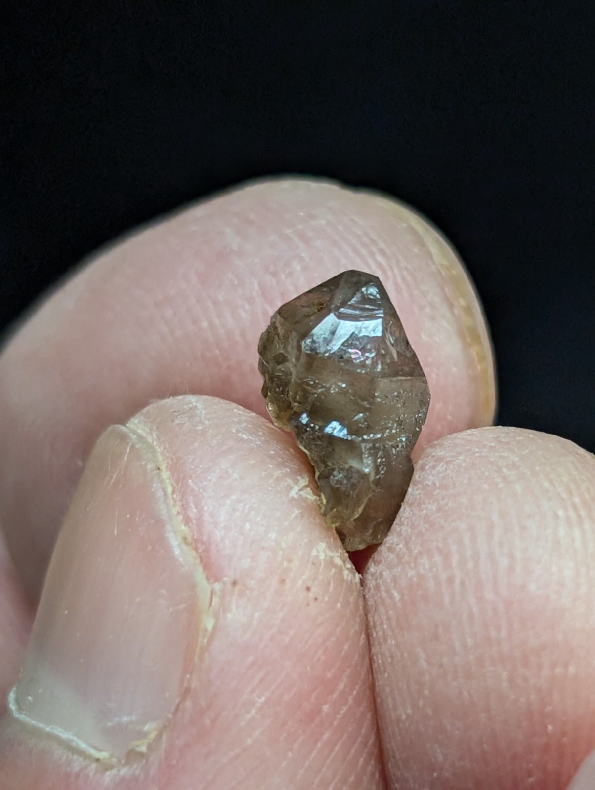 A translucent brown crystal with a faceted, pointed tip held between fingers.
