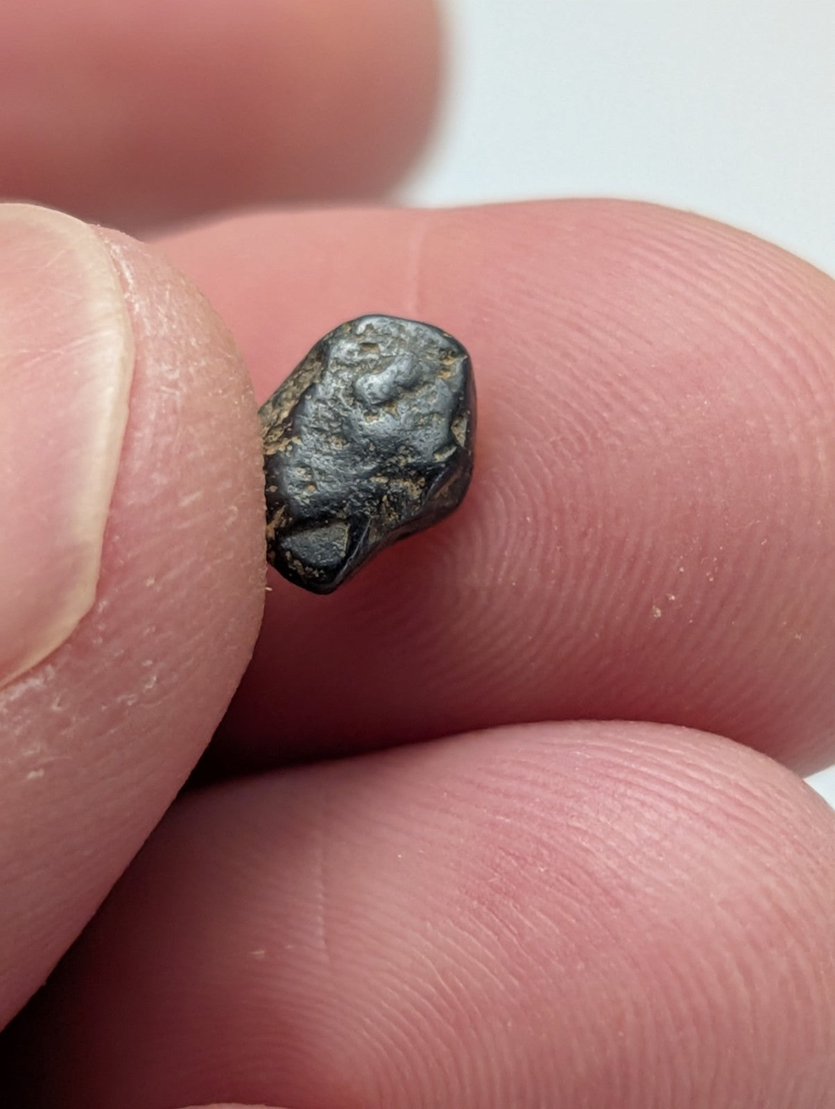 A small irregularly shaped black placer rutile meteorite from magnet cove arkansas held between fingers