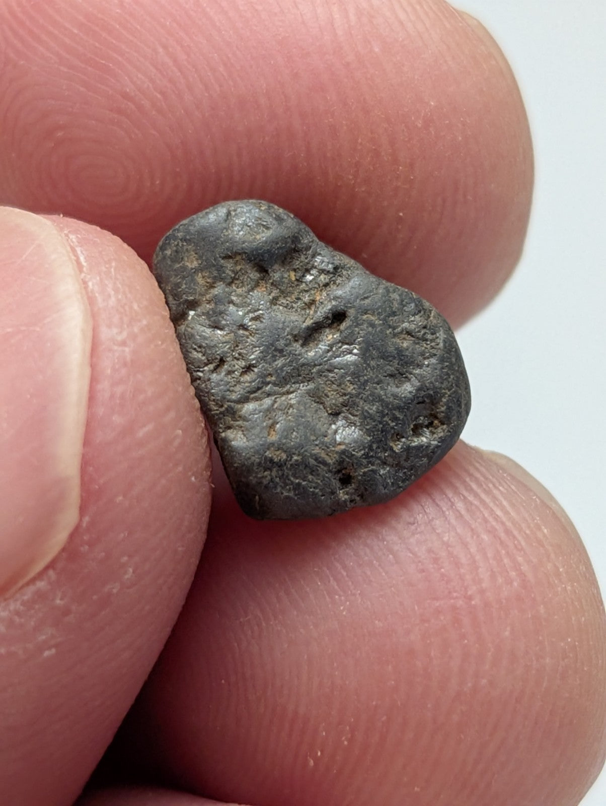 A very rare dark irregular placer rutile meteorite fragment from magnet cove arkansas held between fingers