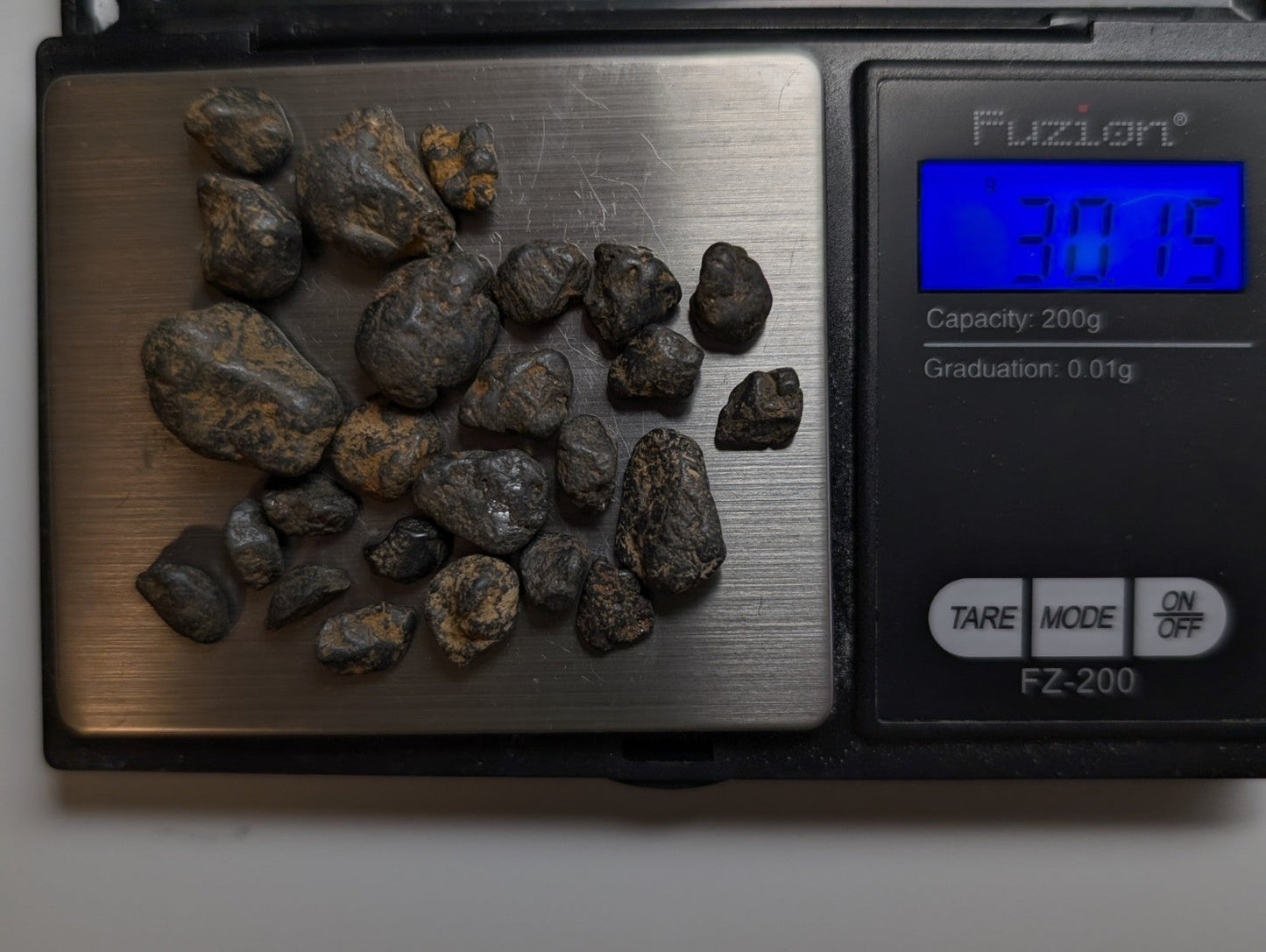 A set of 25 very rare placer rutile dark rough-textured rocks with brown patches on a digital scale from magnet cove arkansas