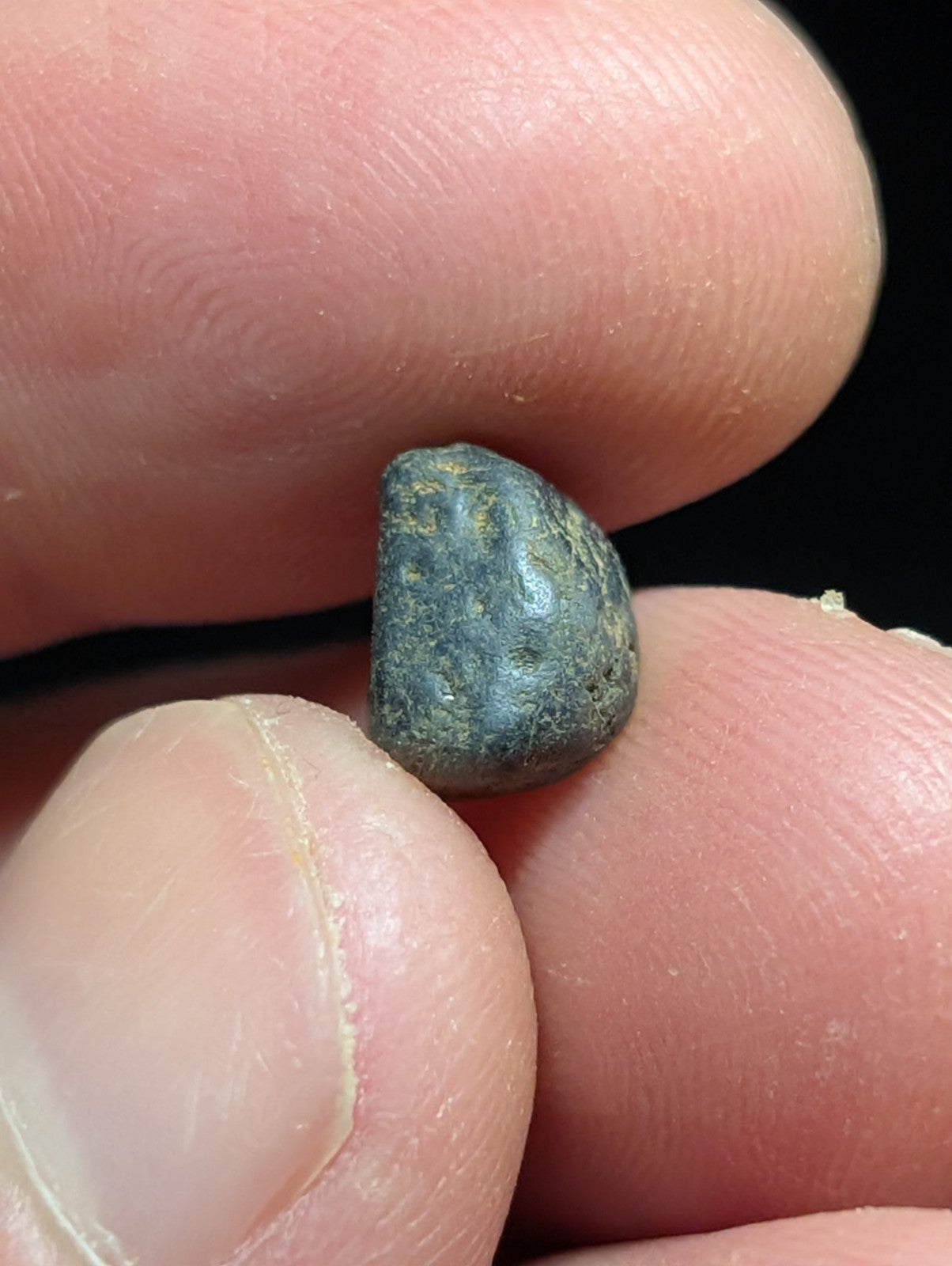 A small, dark greenish-blue patinated bronze coin held between fingers.