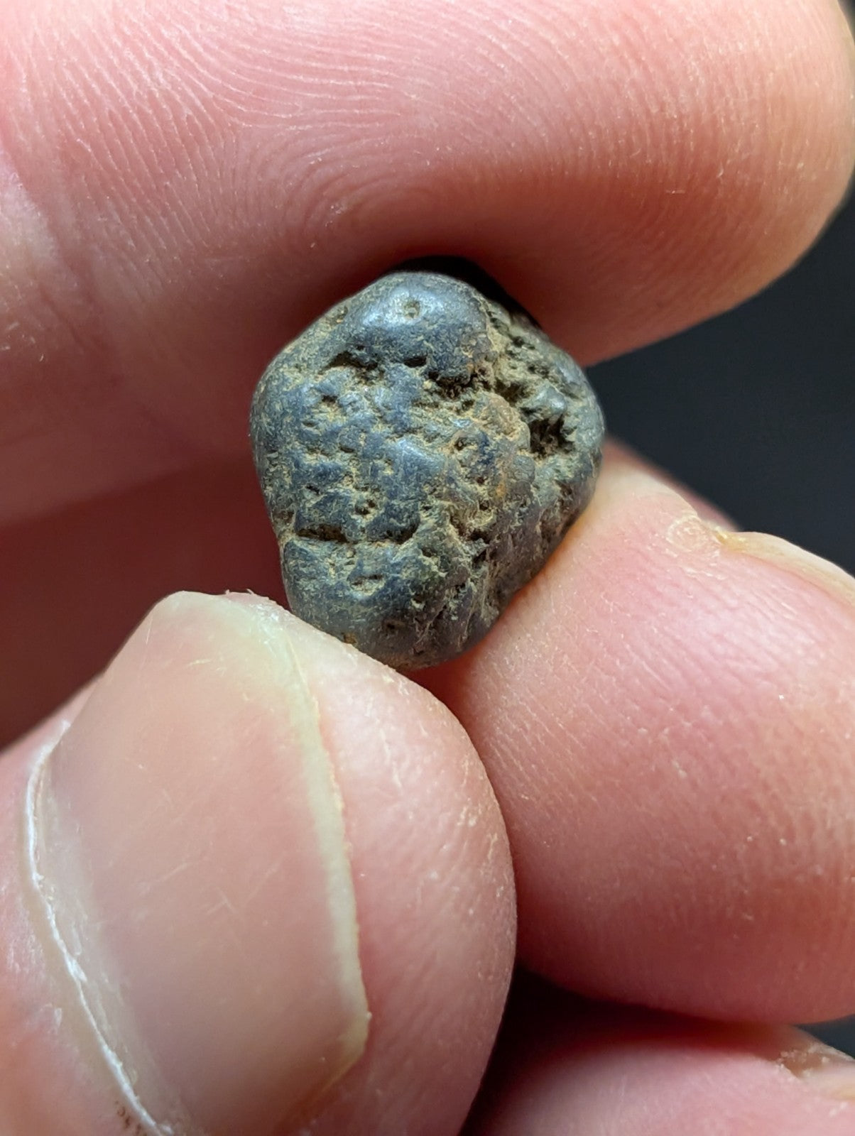 A weathered, dark greenish-gray metallic object with a rough, irregular surface and visible patina.