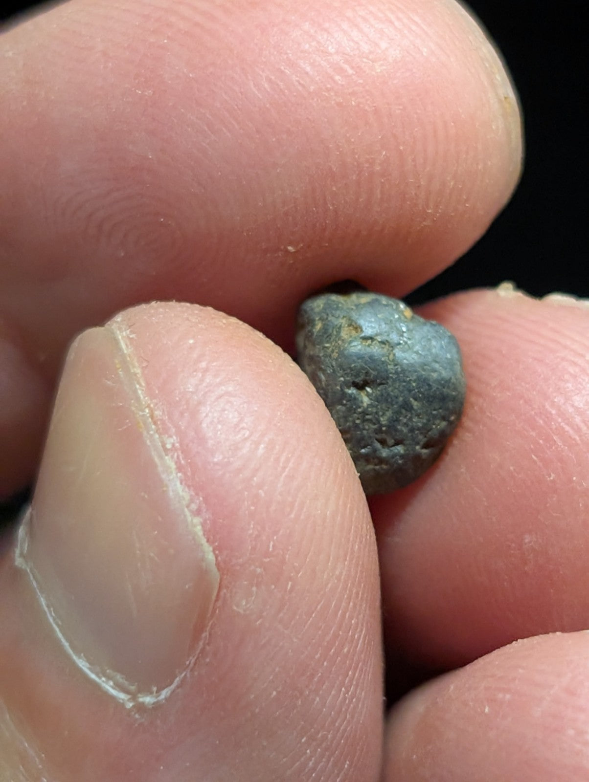 A small, irregularly shaped metallic object with a dark grayish-blue patina and rough texture.