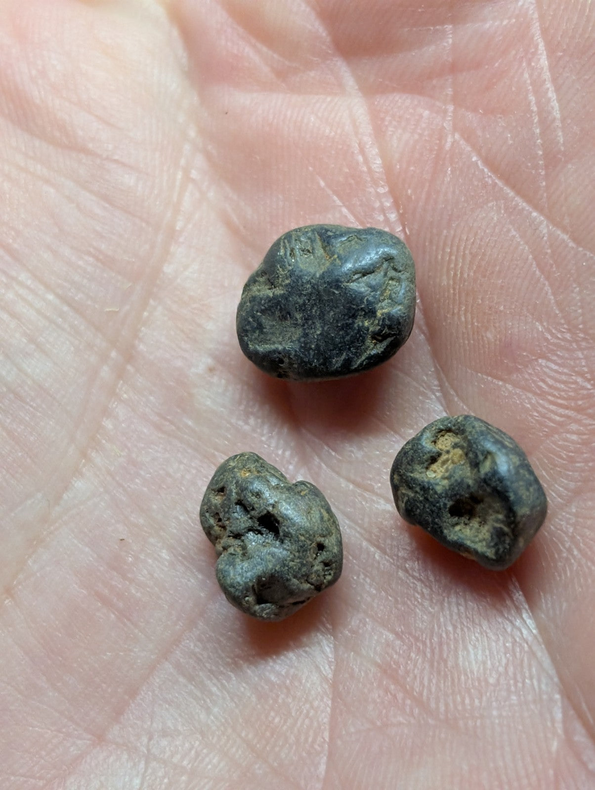 Three dark, irregularly shaped metallic objects with a rough texture and some greenish patina rest in the palm of a hand.