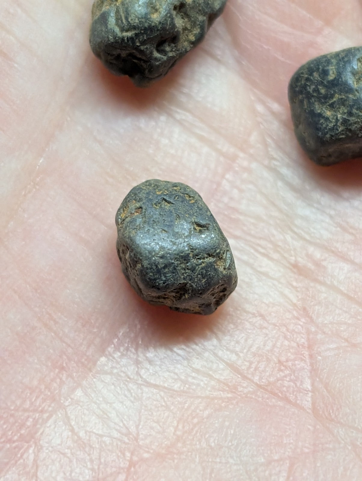 Dark, irregularly shaped metallic pebbles resting on a hand.