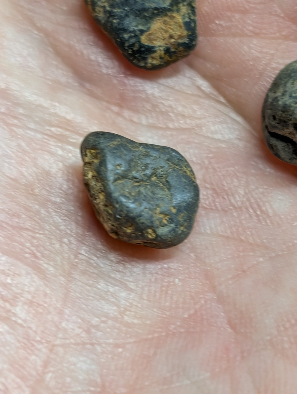 Dark, irregularly shaped stones with patches of yellowish mineral streaks resting in a palm.