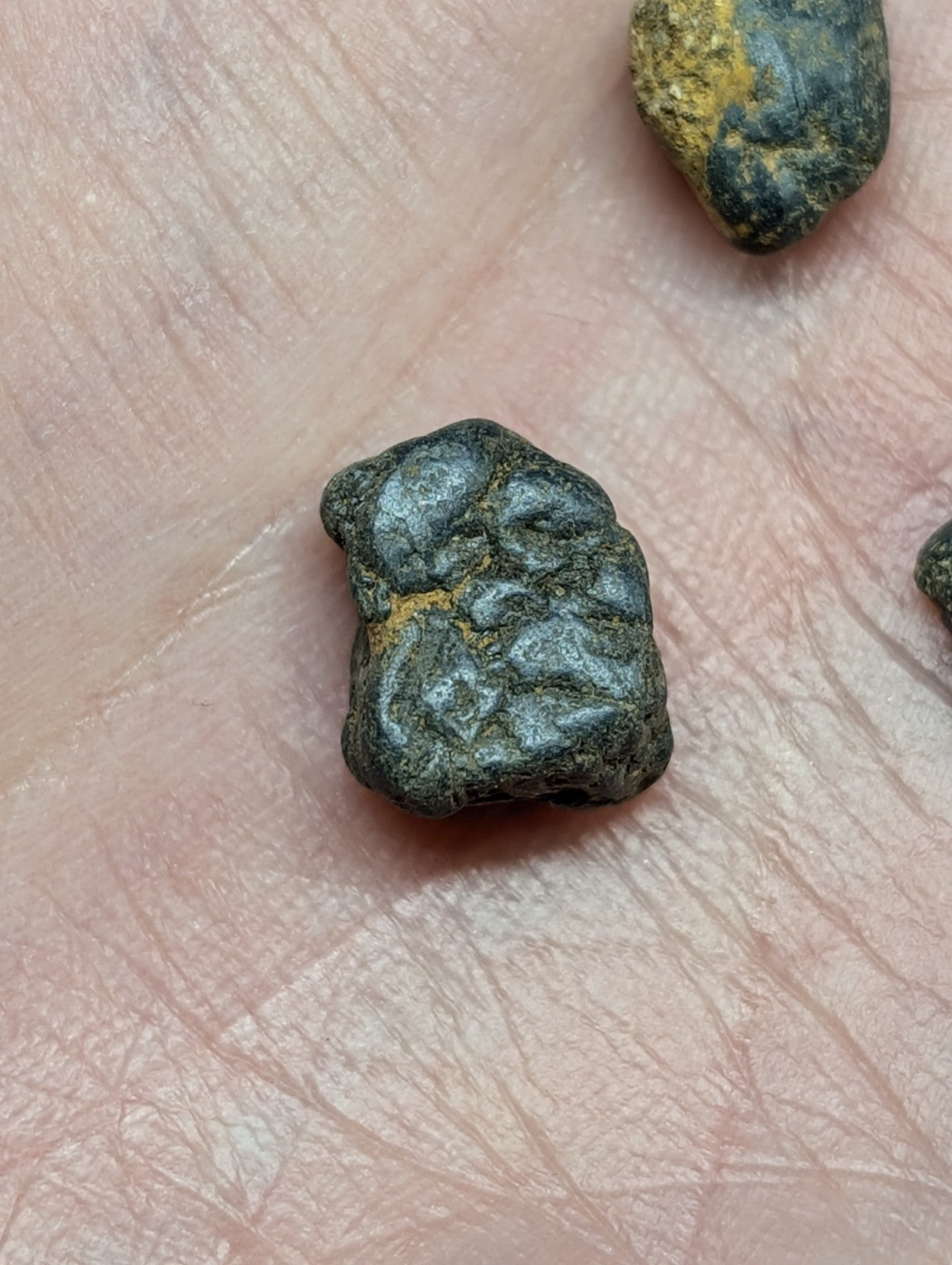 A dark, irregularly shaped stone with a rough texture and patches of yellowish mineral streaks.