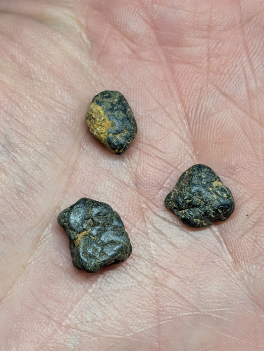 Three dark, irregularly shaped stones with patches of yellowish mineral streaks resting in the palm.