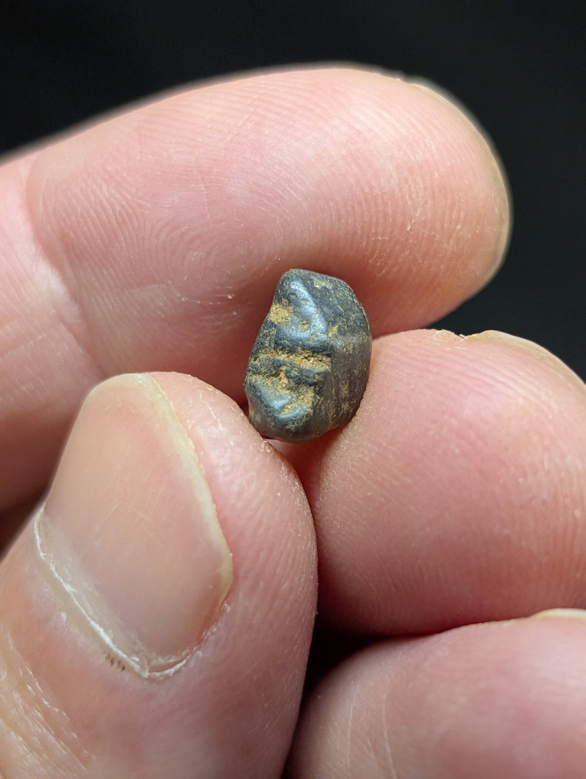 A small, dark gray metallic coin with a weathered surface and faint golden markings.