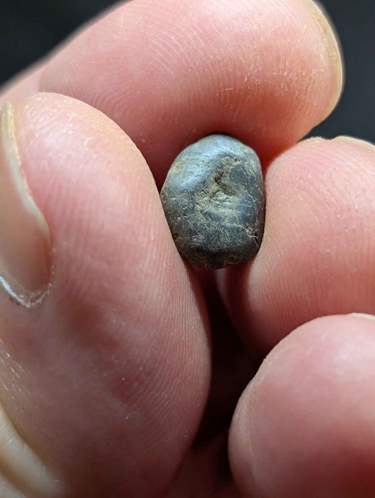 A small, dark gray, irregularly shaped stone held between fingers.