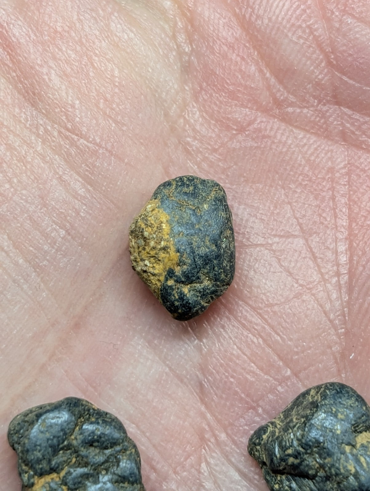 A small, irregularly shaped stone with a dark greenish-blue base and patches of yellow-orange mineral coating.