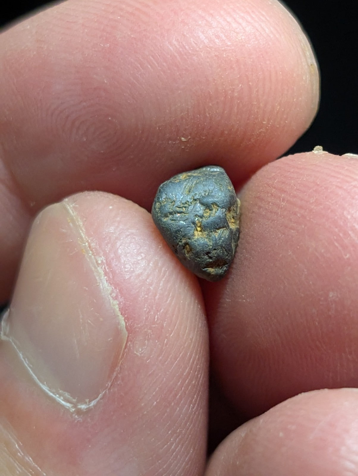 A small, irregularly shaped metallic object with a dark greenish-blue patina and patches of yellowish mineral deposits.