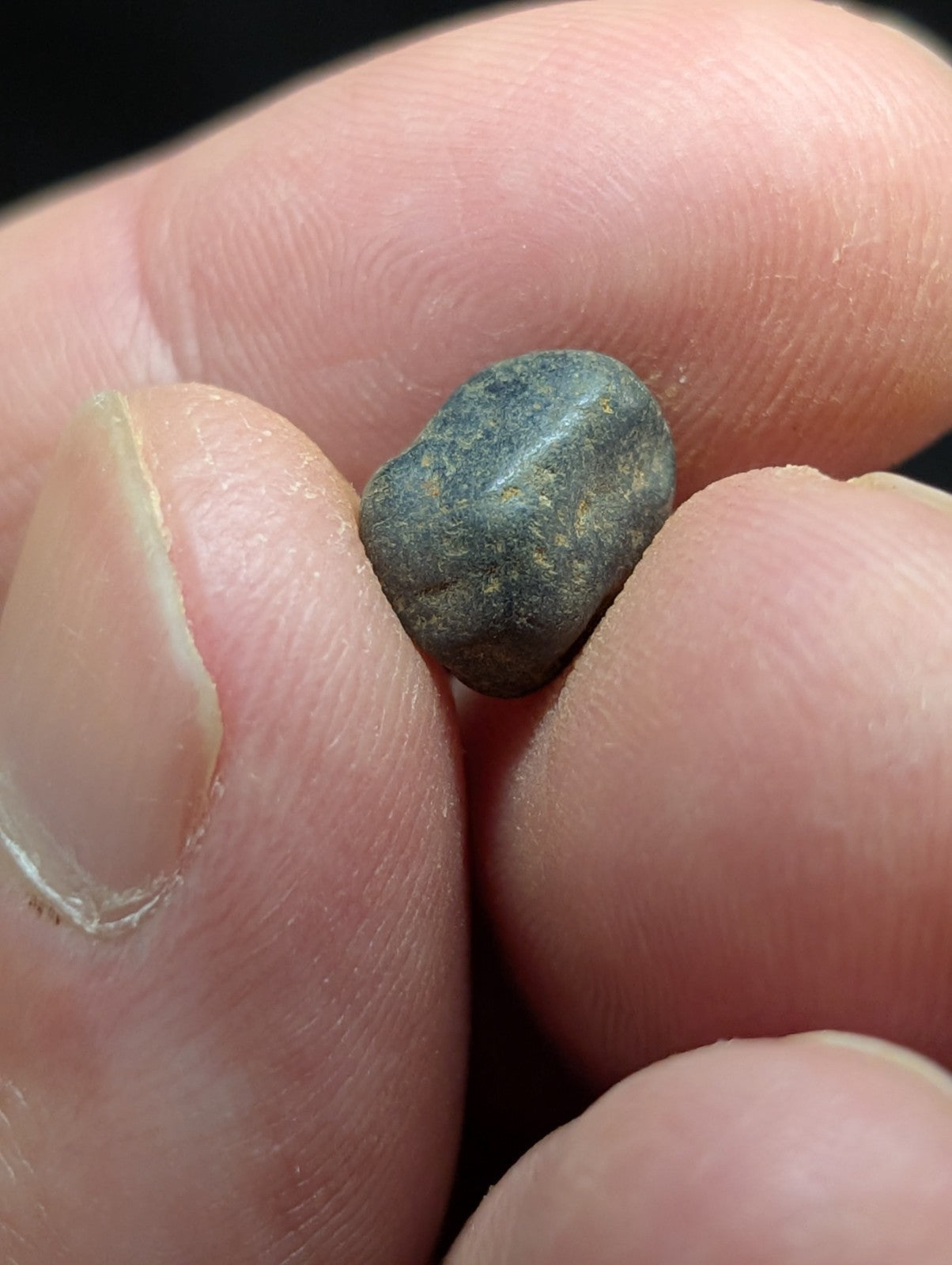 A small, dark greenish-gray stone with a smooth, rounded surface and subtle natural markings.