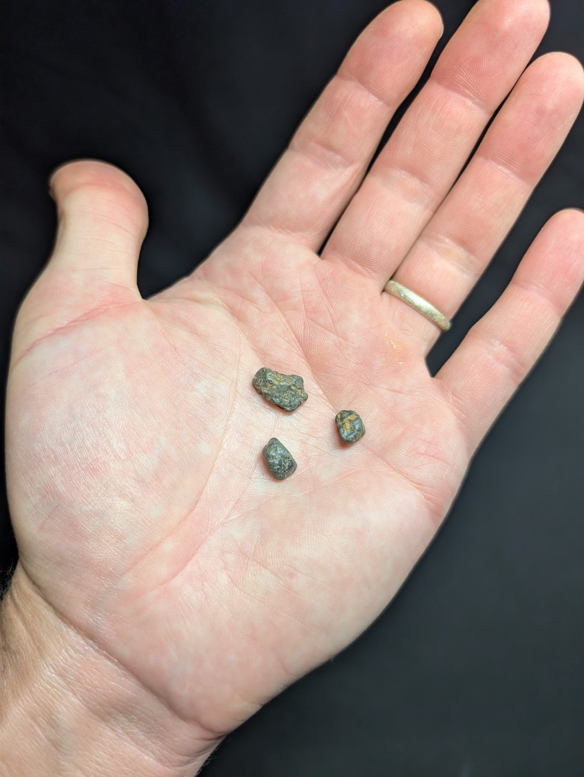 Three small, irregularly shaped greenish-gray stones rest in the palm of a hand.