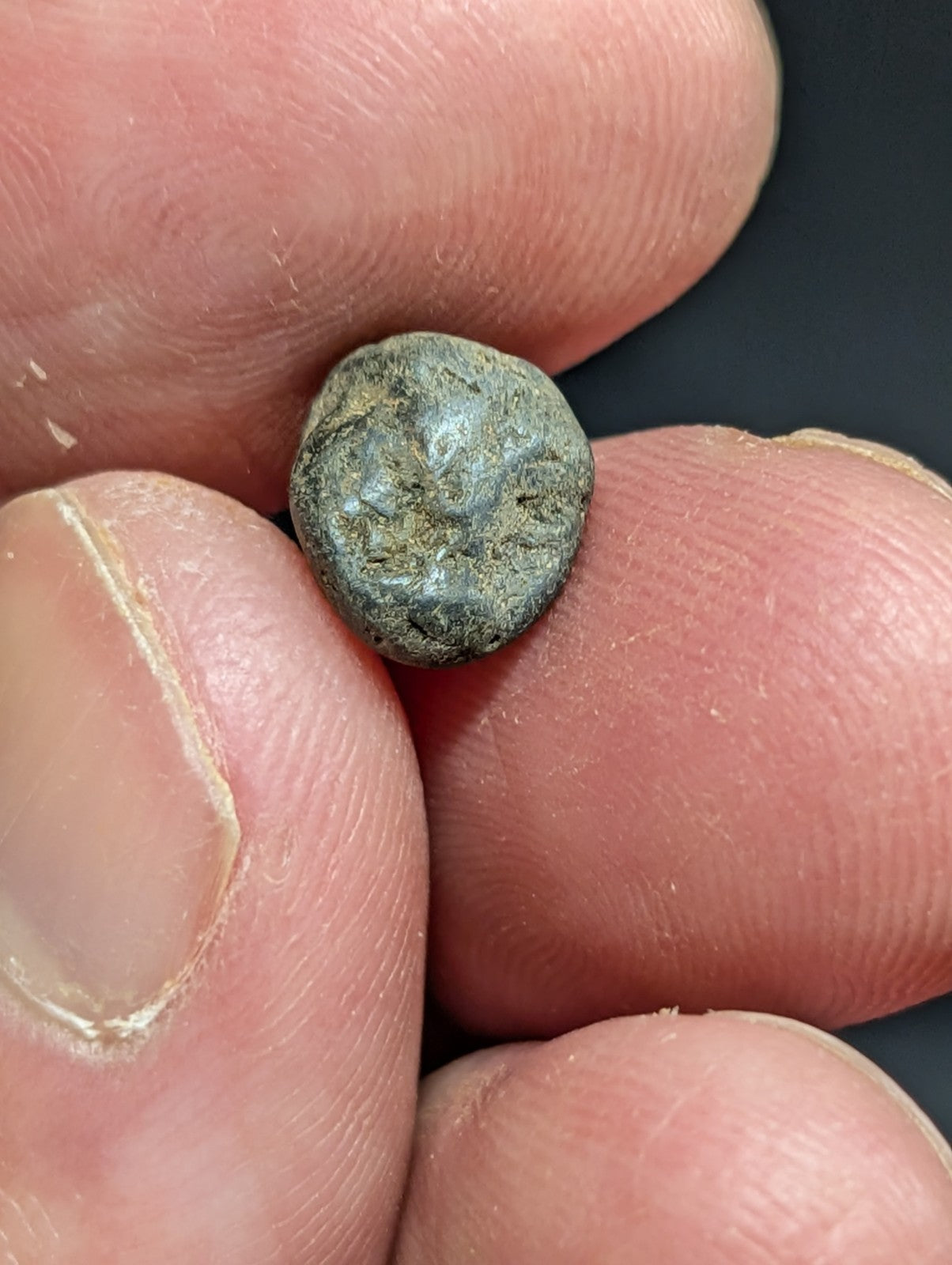 A weathered, dark greenish-gray ancient coin held between fingers.