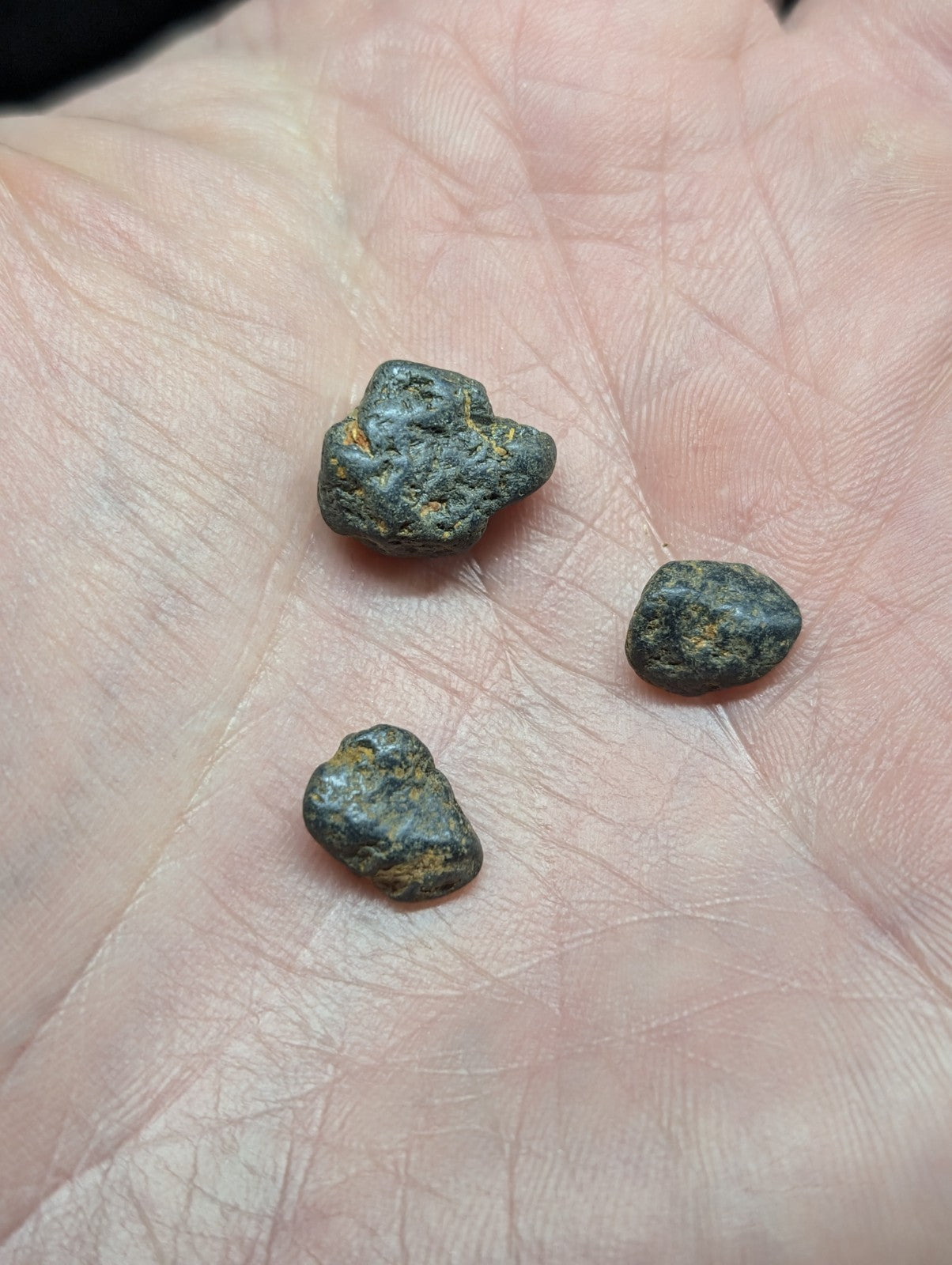 Three small, irregularly shaped dark green and black rocks with patches of yellowish mineral streaks rest in the palm.