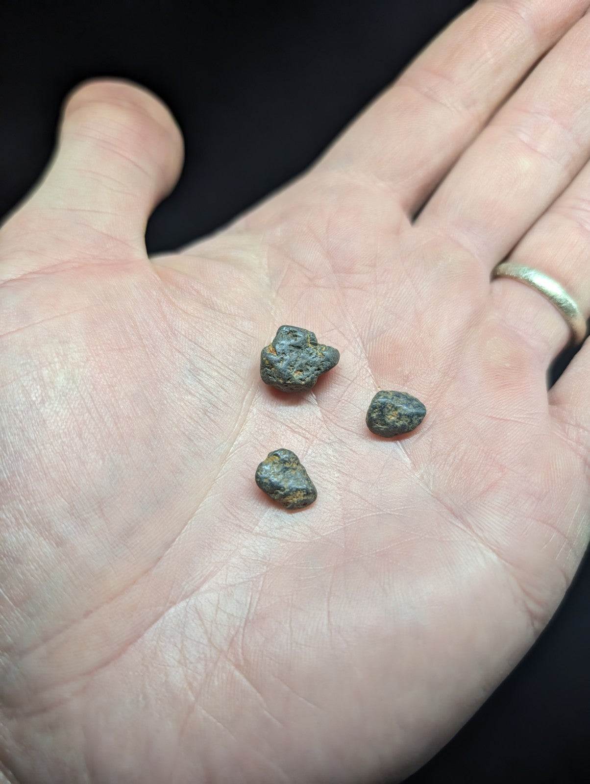 Three small, irregularly shaped dark green and brown metallic fragments rest in the palm of a hand.