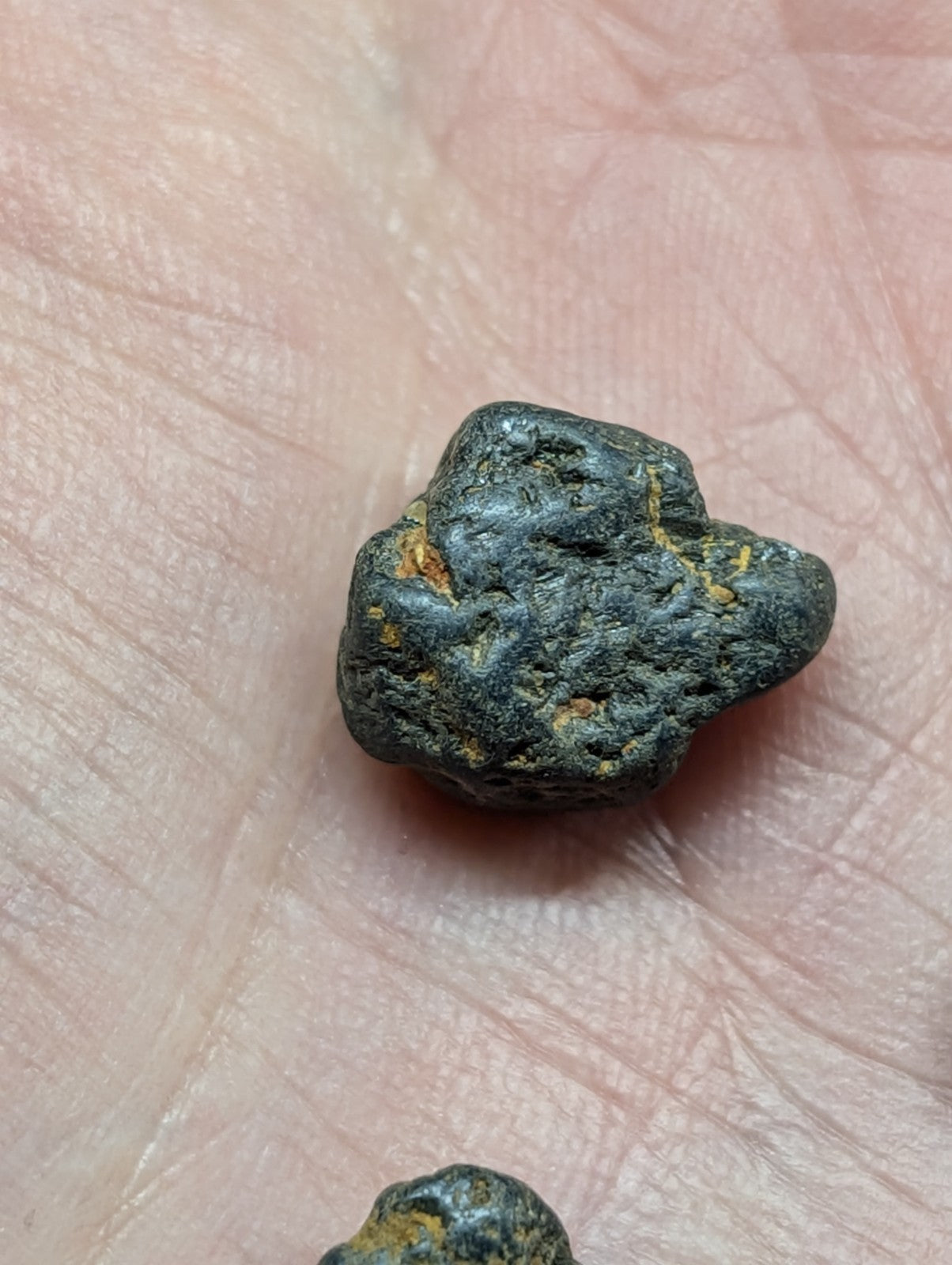 A dark, rough-textured mineral specimen with patches of yellowish oxidation resting on a human palm.