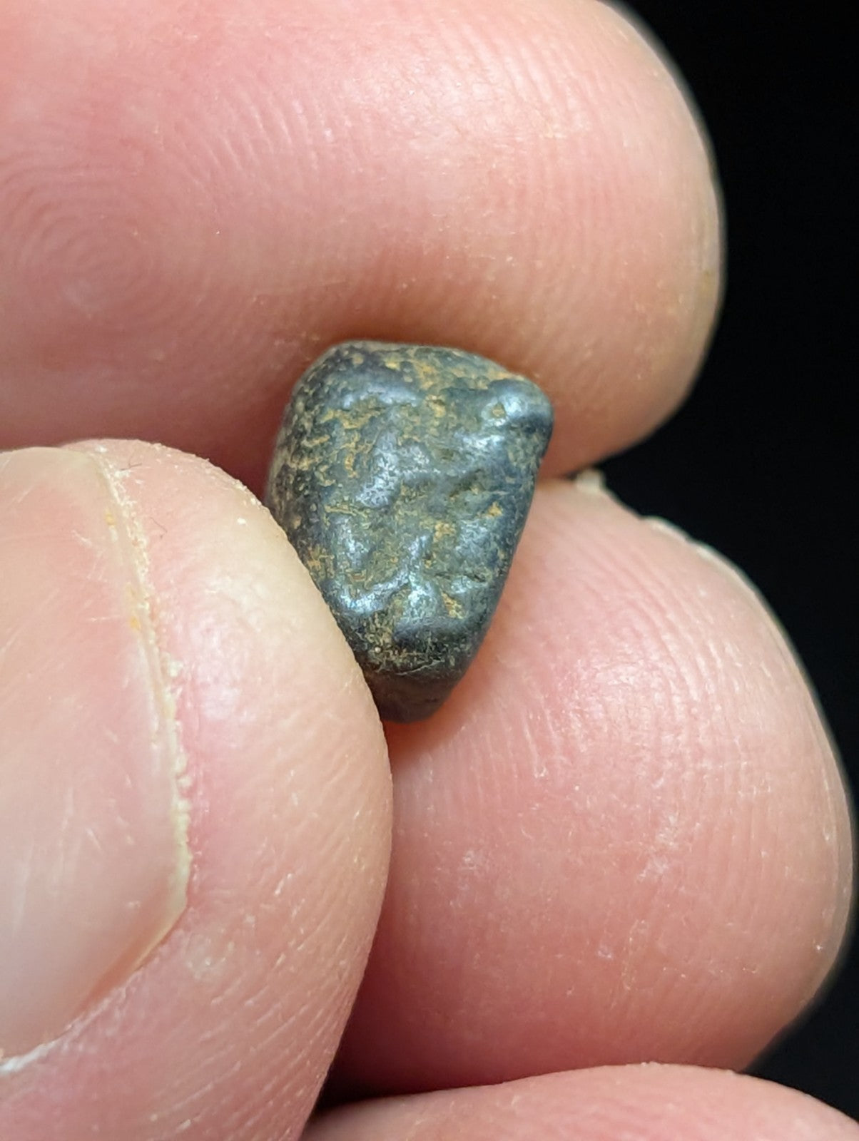 A small, irregularly shaped bronze coin with a dark green patina and visible surface texture.