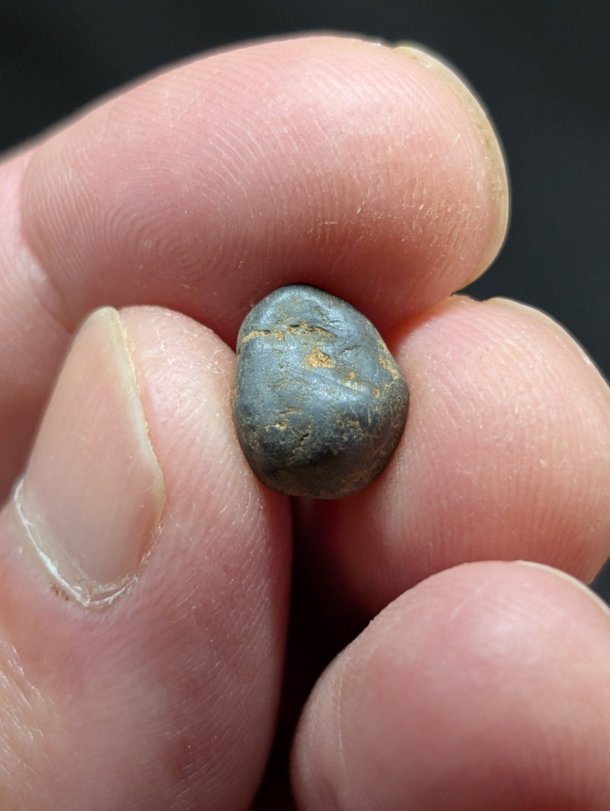 A smooth, dark gray pebble with subtle golden speckles held gently between fingers.