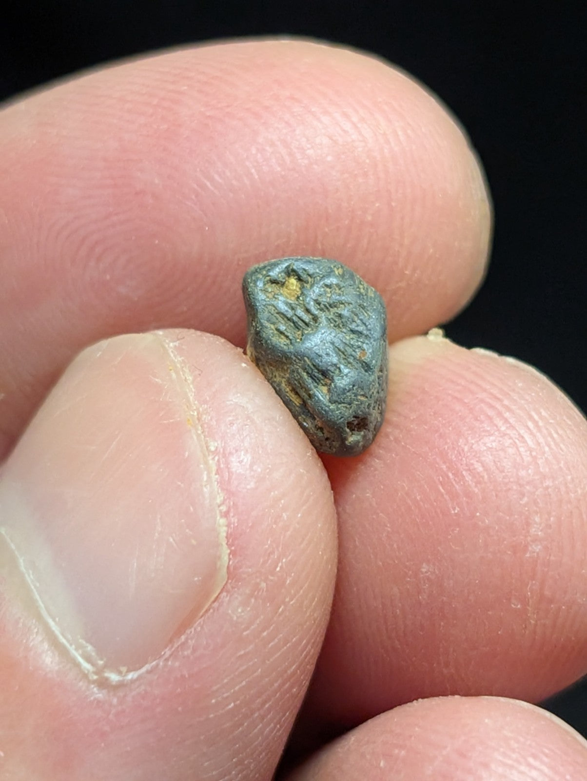 A small, irregularly shaped metallic object with a greenish-blue patina and faint yellow markings.