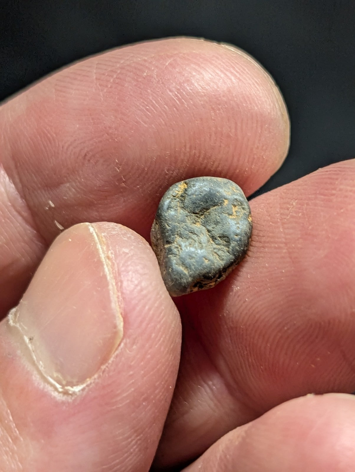 A small, irregularly shaped stone with a mottled greenish-blue surface and patches of yellow patina.