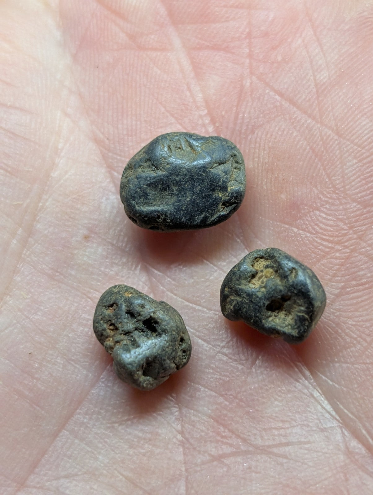 Three weathered, dark greenish-gray metallic coins with rough, irregular surfaces and visible signs of oxidation rest in the palm.