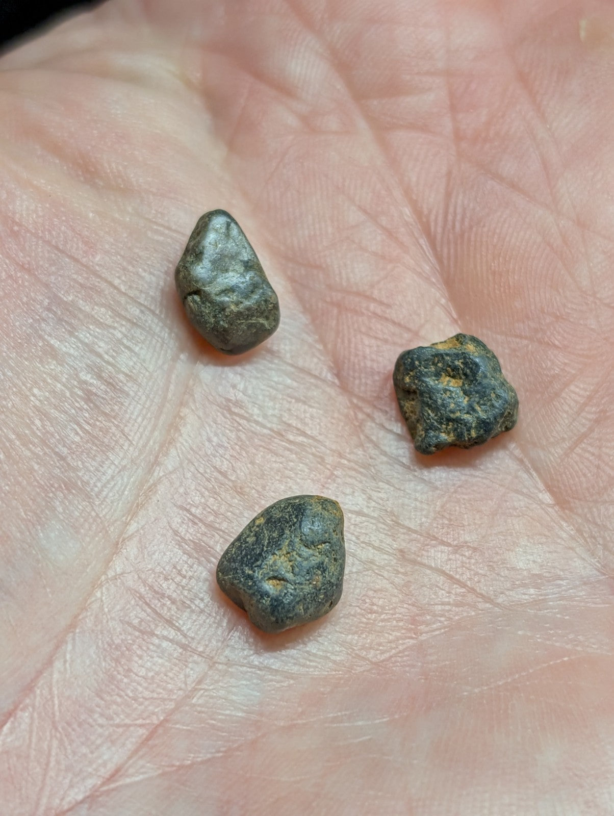 Three small, irregularly shaped dark green and black stones with rough textures rest in the palm of a hand.