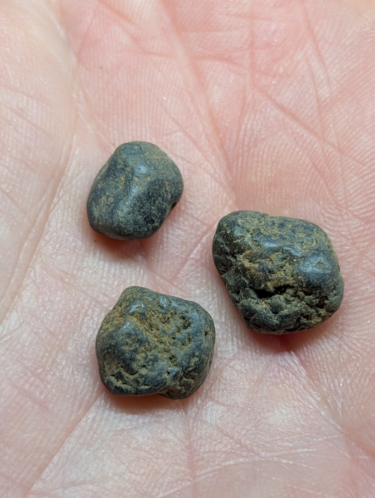 Three dark, weathered copper coins with rough, irregular surfaces rest in the palm of a hand.