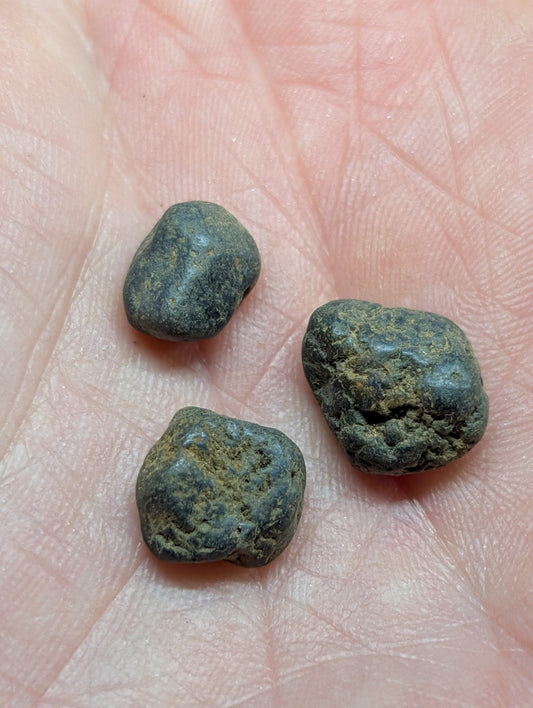 Three dark, weathered copper coins with rough, irregular surfaces rest in the palm of a hand.