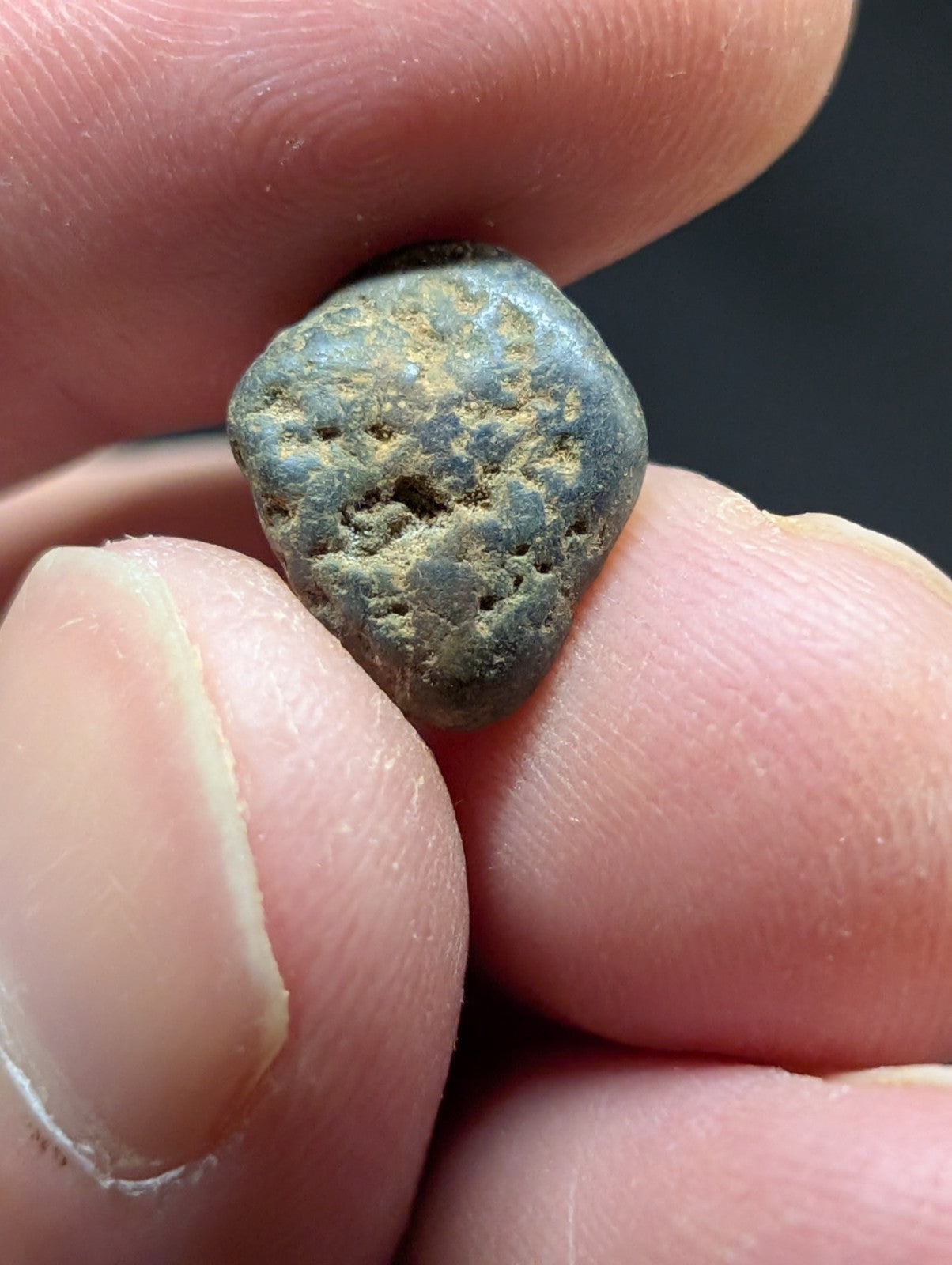 A weathered, irregularly shaped metallic object with a greenish patina and speckled surface.