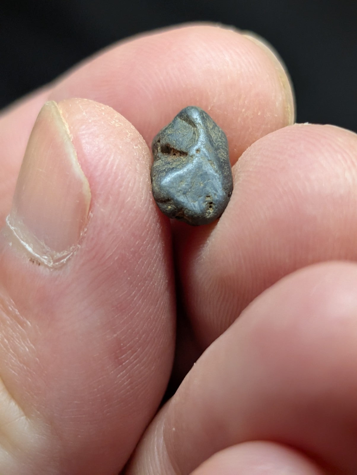 A small, irregularly shaped gray meteorite fragment with a slightly rough texture and subtle surface markings.