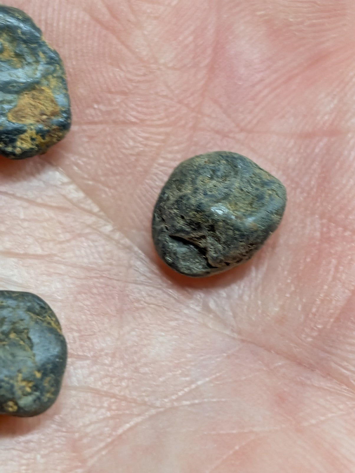 Dark green, rough-textured stones with patches of yellowish mineral streaks rest in the palm.