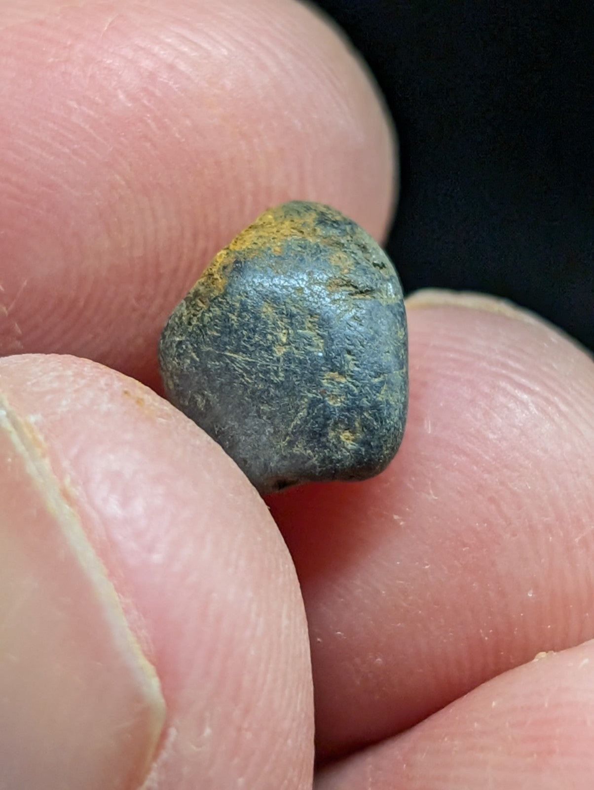 A dark, smooth pebble with a glossy surface and patches of yellowish rust.