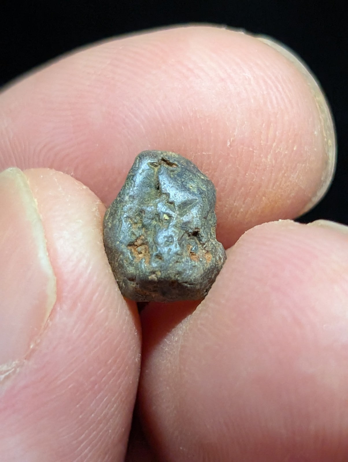 A small, irregularly shaped metallic object with a dark gray patina and hints of rust-colored oxidation.