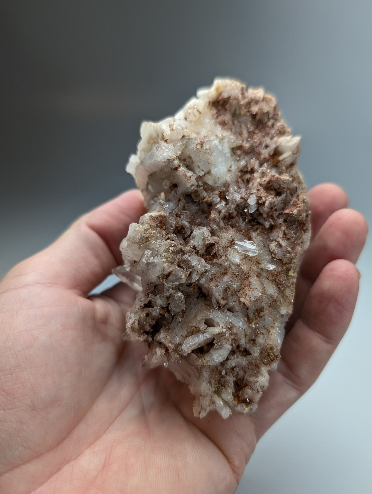 A hand holds a very unique faden quartz crystal cluster with translucent white and brownish minerals from Arkansas USA